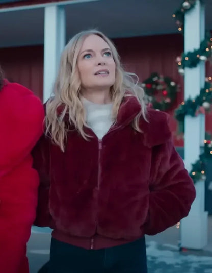 Woman in maroon faux fur jacket standing outside with Christmas wreath decorations