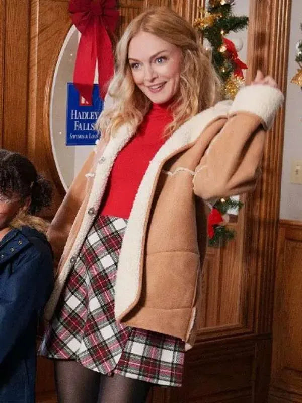 Woman in tan shearling jacket, red top, and plaid skirt at Christmas indoor setting
