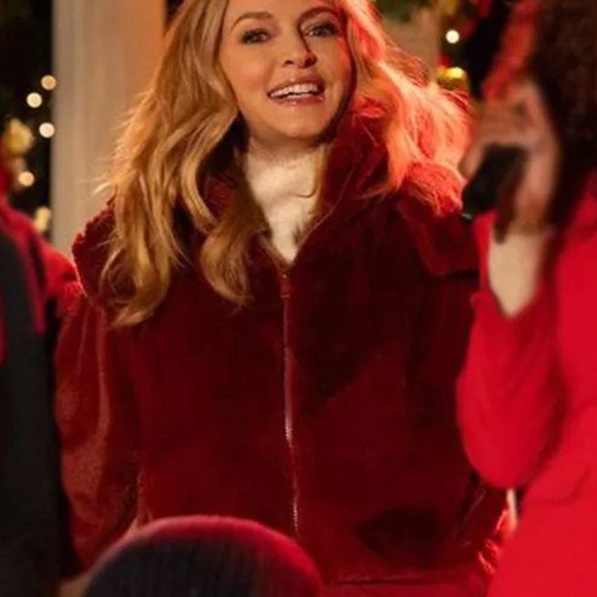 Woman in maroon jacket smiling at Christmas event with festive lights in background