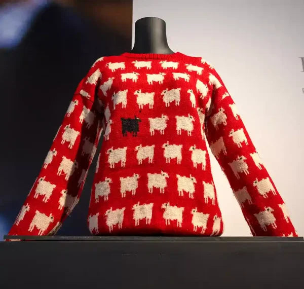 Red Christmas sweater with white sheep pattern and one black sheep on a mannequin display.