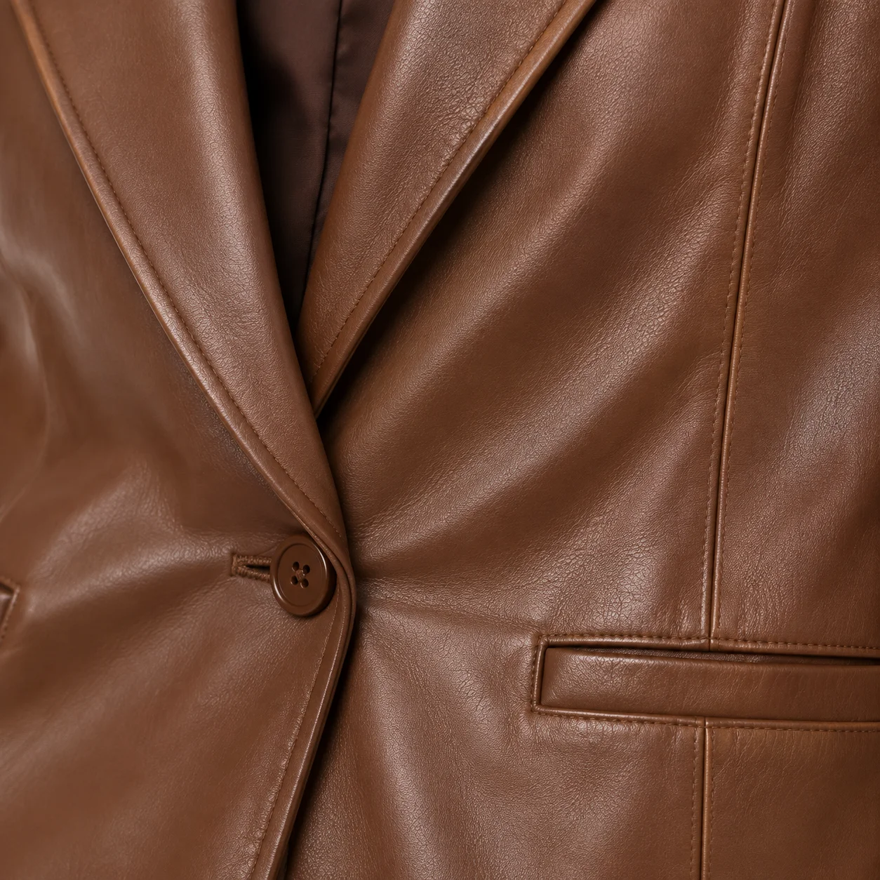 Close-up of caramel brown Nappa lamb leather showing smooth natural grain, lapel, stitching, button and welt pocket detail