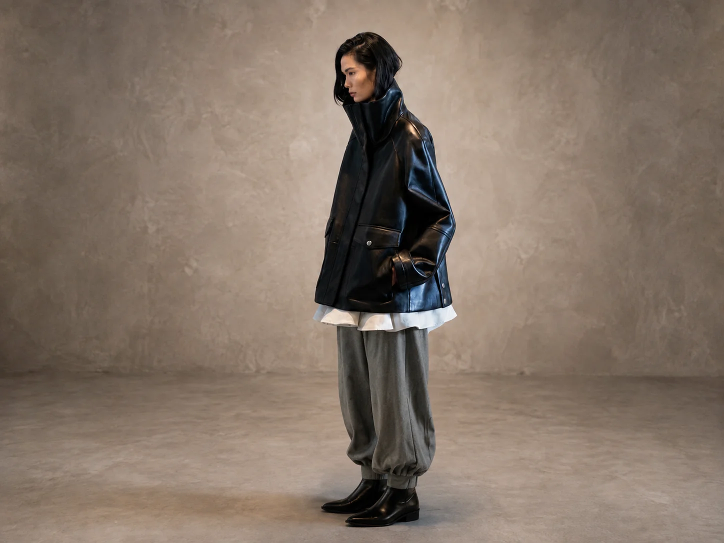 Side view of woman styling an oversized funnel-neck leather coat with layered outfit